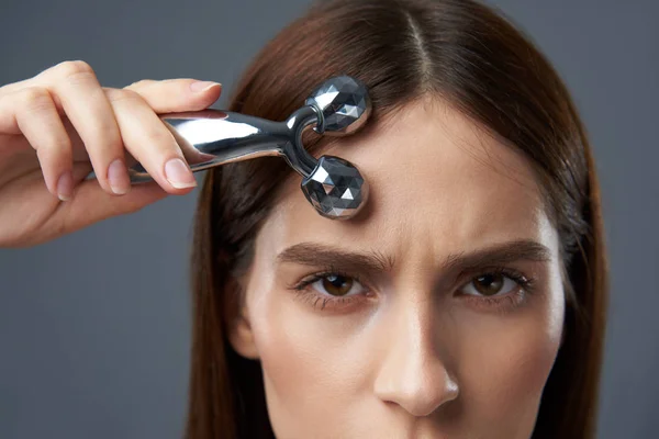 Beautiful brunette girl using platinum facial massager — Stock Photo, Image