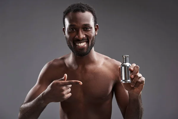 Cintura para cima de um homem afro-americano alegre mostrando seu perfume — Fotografia de Stock