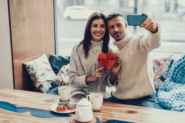 Two person sitting in cafe with present and making selfie