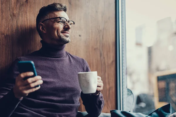Homme avec cellulaire et tasse dans les mains assis dans le café — Photo