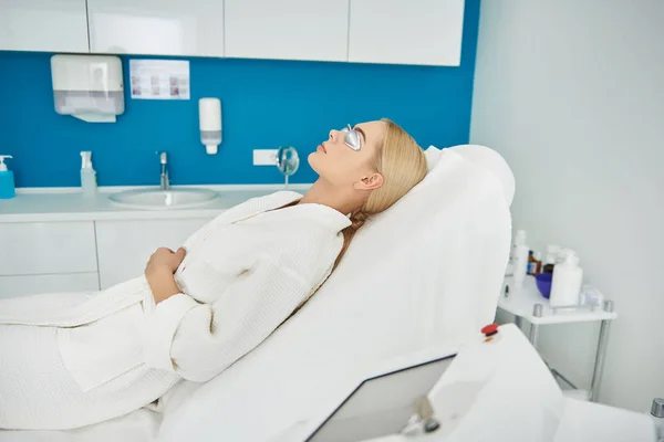 Menina bonita em roupão descansando no armário cosmetologist antes do procedimento — Fotografia de Stock