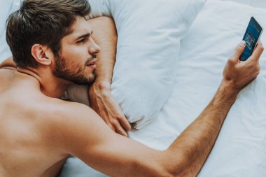 Genç adam cep telefonu ile yatakta döşeme