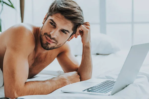 Pensativo chico joven usando el ordenador portátil en la cama — Foto de Stock