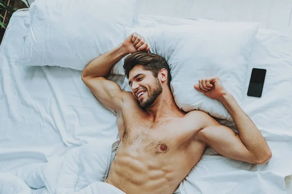 Счастливый молодой парень растягивается в постели дома — стоковое фото
