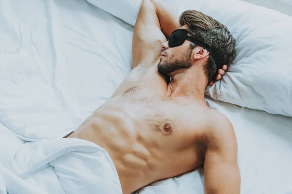 Молодой привлекательный мужчина лежал с повязкой на глазах в постели — стоковое фото
