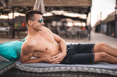 Güneş şezlong üzerinde rahatlatıcı ve gülümseyerek emin gömleksiz adam