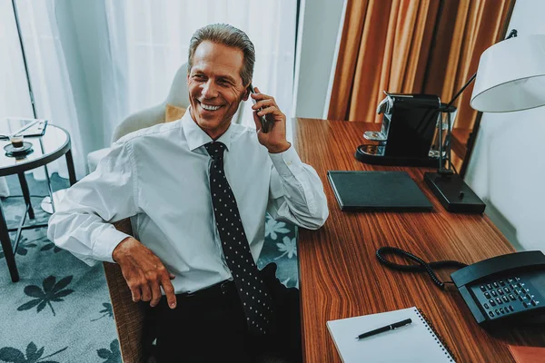Örömmel üzletember beszél a telefonon az asztalnál ülve — Stock Fotó