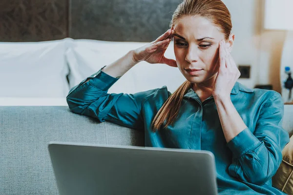 Poważne kobiety dotykając jej świątynie, patrząc na laptopa — Zdjęcie stockowe