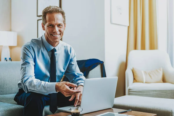 Cheerful adult man in shirt and tie sitting with laptop and smiling — Stock Photo, Image