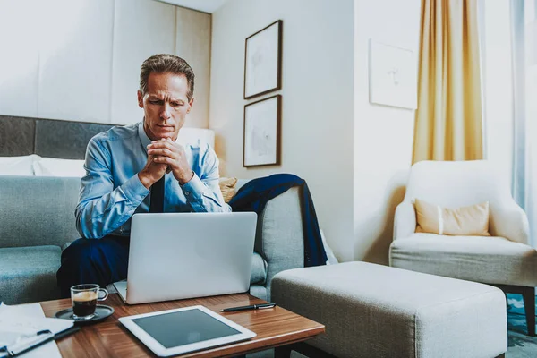 Allvarlig vuxen man rynkar pannan medan sitta framför den bärbara datorn — Stockfoto