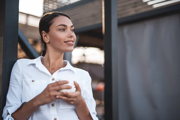 Dreamy lady looking away and smiling while drinking coffee