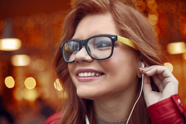 Vonzó a vörös hajú lány a szemüveg használata fülhallgató — Stock Fotó