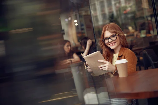 Hermosa chica pelirroja leyendo libro en la cafetería al aire libre — Foto de Stock