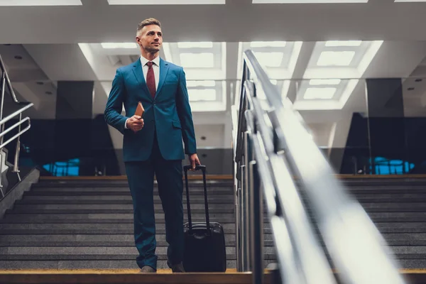 Hombre guapo con maleta en las escaleras mirando a un lado — Foto de Stock