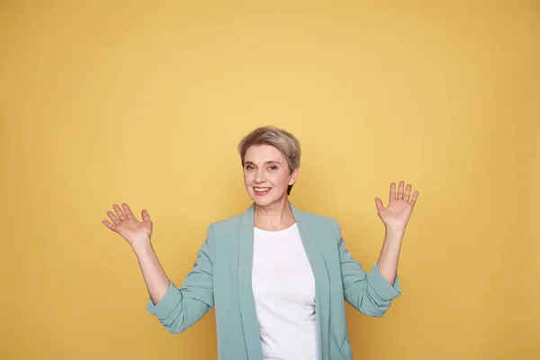 Feliz mãe encantadora levantando as mãos no fundo amarelo — Fotografia de Stock