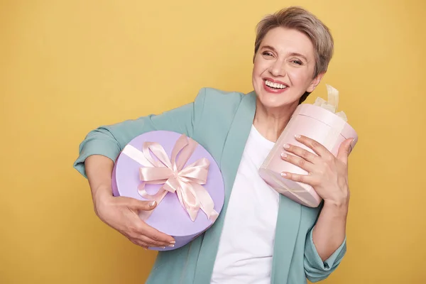 Half length of happy beautiful mother holding presents on yellow background — Stock Photo, Image