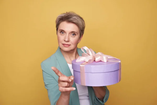 Half length of serious mother holding present on yellow background — Stock Photo, Image