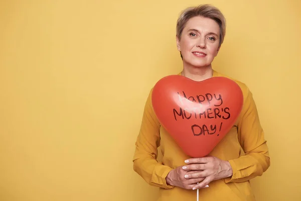 Waist up of calm woman holding red heart shaped balloon in arms — Stock Photo, Image