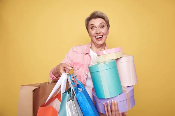 Waist up of happy beautiful mother holding presents on yellow background — Stock Photo, Image