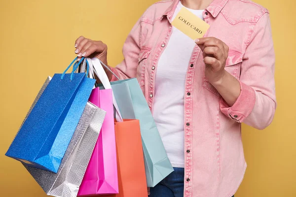 Foto recortada de la mano femenina sosteniendo coloridas bolsas de compras y tarjeta de oro —  Fotos de Stock