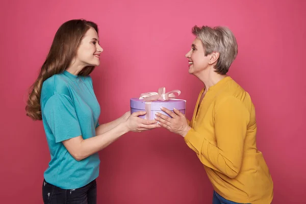 Side view of happy brown-haired girl giving to her mother a present