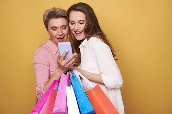 Waist up of happy women looking at screen of smartphone after shopping — Stock Photo, Image