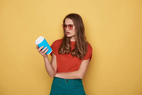 Taille des nervösen Mädchens hält Cupholder im Arm vor orangefarbenem Hintergrund — Stockfoto