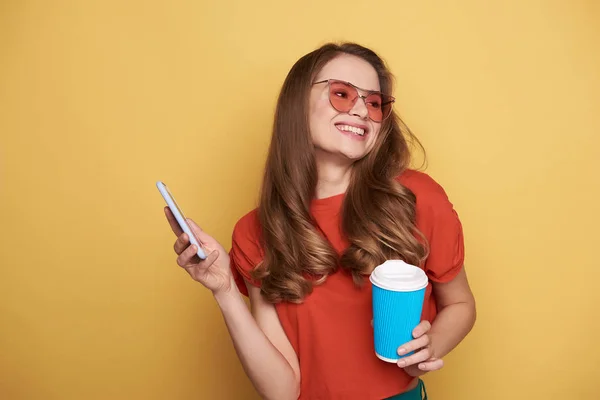 Brune souriante jeune femme aux lunettes tenant son téléphone portable et buvant du café — Photo