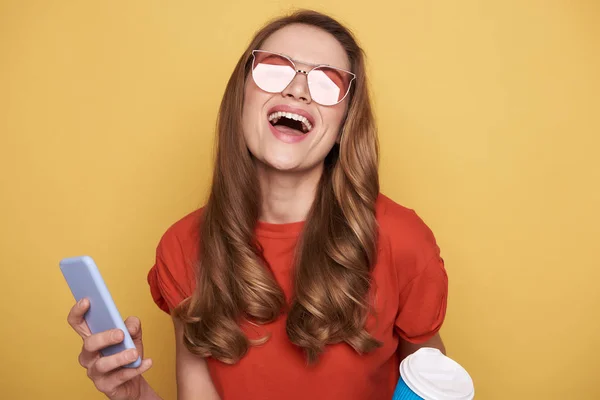 Lachen brunette meisje in brillen houden cellphone en koffie drinken — Stockfoto