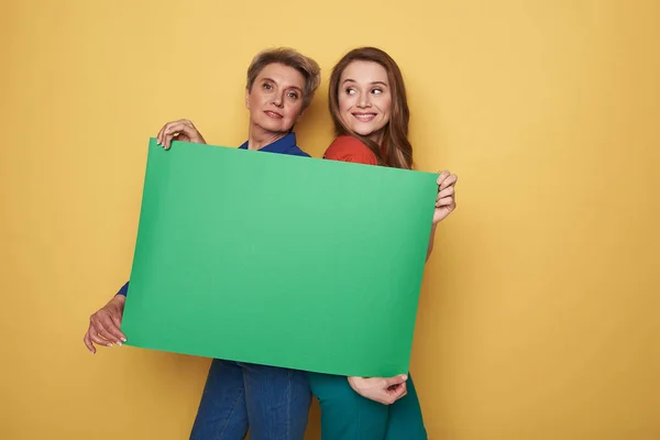 Обрізаний фото кавказьких жінок, тримаючись за зелений порожній плакат студії — стокове фото