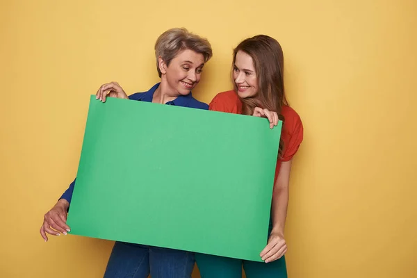 Foto recortada de mulheres caucasianas segurando cartaz verde vazio em estúdio — Fotografia de Stock