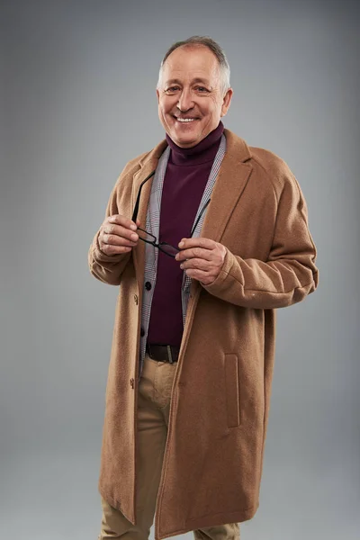 Cheerful man in long coat standing alone and holding glasses — Stock Photo, Image