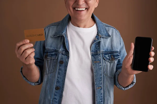 Close up of gold card and modern gadget in hands of smiling man