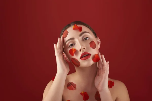 Krásná žena, která jí sahala po obličeji s plátky růží — Stock fotografie
