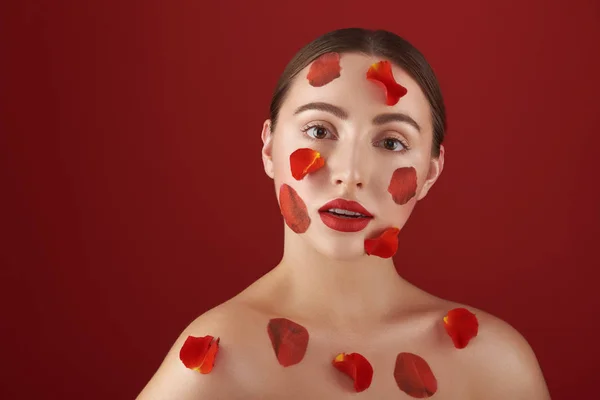 Donna premurosa con labbra rosse con petali di rosa sul viso e sul corpo — Foto Stock