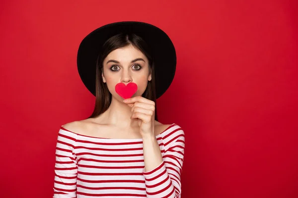 Hübsches Mädchen, das die Lippen durch rotes Papierherz schließt — Stockfoto