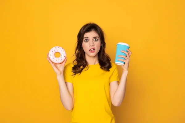 Junges verwirrtes Mädchen mit Donut und Kaffee — Stockfoto
