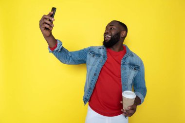 Waist up of smiling African man keeping cupholder and smartphone in arms clipart