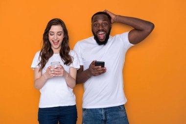 Beyaz tişörtler içinde yarım uzunlukta ırklar arası çift kollarında akıllı telefonlar tutan