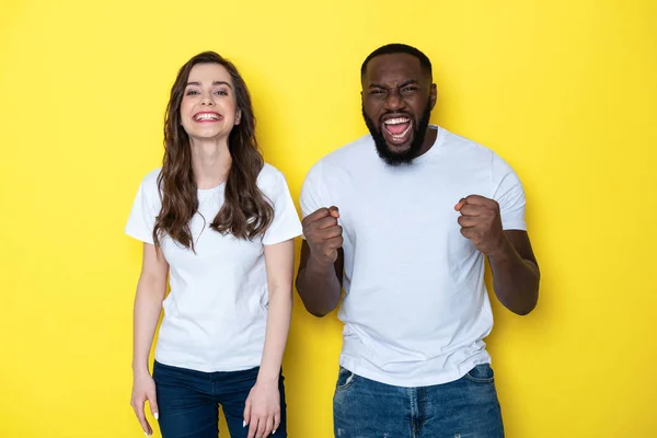 Sorpreso fortunato interrazziale coppia in bianco T-shirt in posa per la fotocamera in studio — Foto Stock