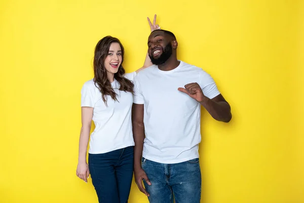 Усміхнена міжрасова пара в білих футболках дивиться на камеру в студії — стокове фото