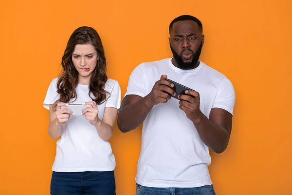 Cropped photo of interracial couple in white T-shirts holding smartphones in arms