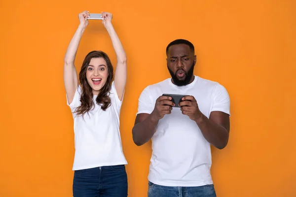 Cropped photo of interracial couple in white T-shirts holding smartphones in arms