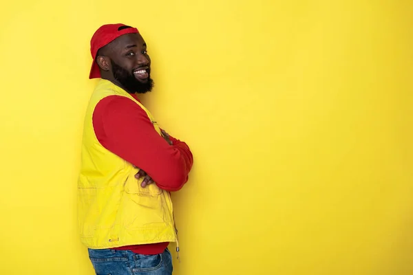 Vista lateral del hombre africano barbudo con las manos cruzadas sobre fondo amarillo — Foto de Stock