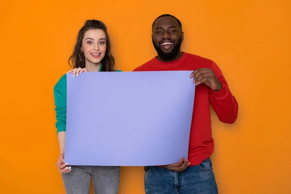 Felice coppia interrazziale in possesso di banner viola vuoto con spazio copia in studio — Foto Stock