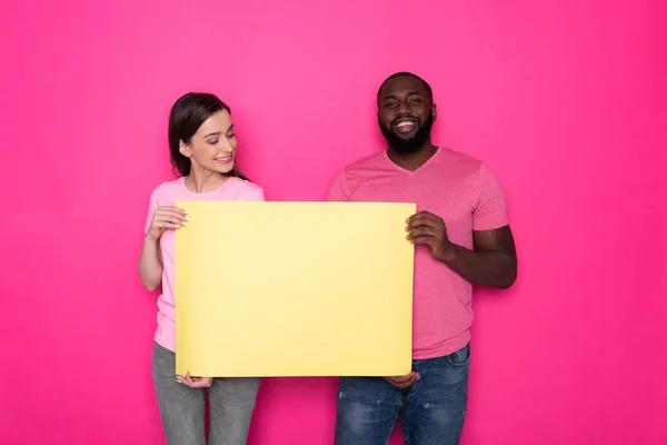 Усміхнена міжрасова пара тримає порожній жовтий банер з копіювальним простором в студії — стокове фото