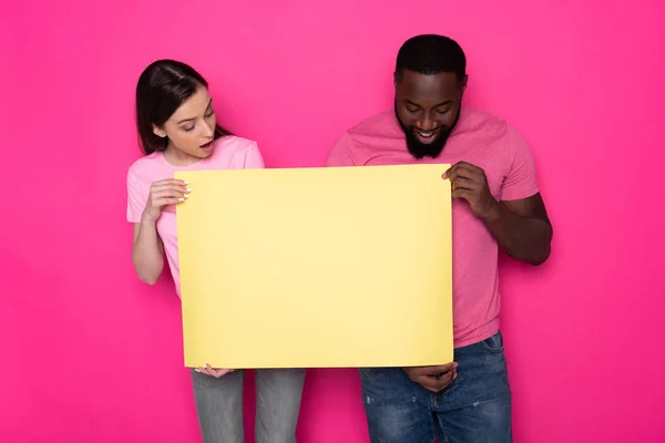 Giovane coppia interrazziale in possesso di banner giallo vuoto con spazio copia in studio — Foto Stock