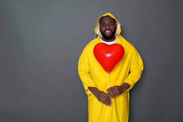 Taille up van gelukkige Afrikaanse man dragen gele regenjas tegen grijze achtergrond — Stockfoto