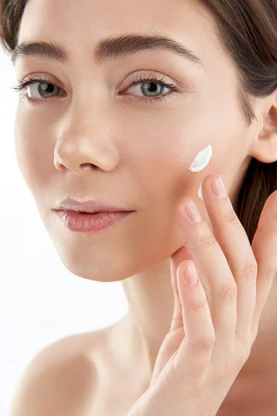 Pretty young female applying cream on cheek — Stock Photo, Image
