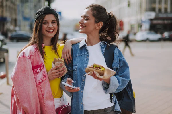 Boldog lányok járkálni város hot dogot — Stock Fotó